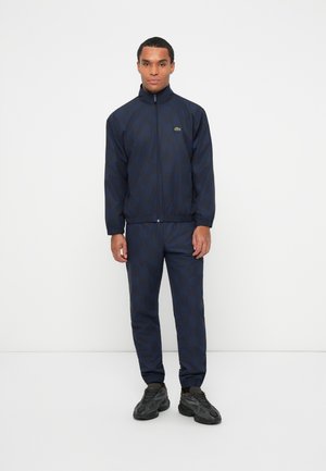 Navy checkered track jacket with a high collar and elastic cuffs, paired with matching pants. Features a small logo on the left chest.