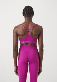 Sujetador deportivo fucsia con tirantes ajustables y banda con logo; combinado con leggings de talle alto a juego, ambos en un tejido liso y elástico.