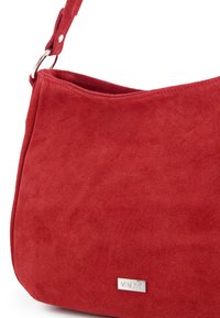 Sac bandoulière en daim rouge avec attache anneau argenté et petite étiquette métallique rectangulaire de marque portant l'inscription « VENEZIA ».