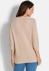 Beiger Pullover mit strukturiertem Strick, Dreiviertelärmeln und rundem Ausschnitt, kombiniert mit blauen Jeans.