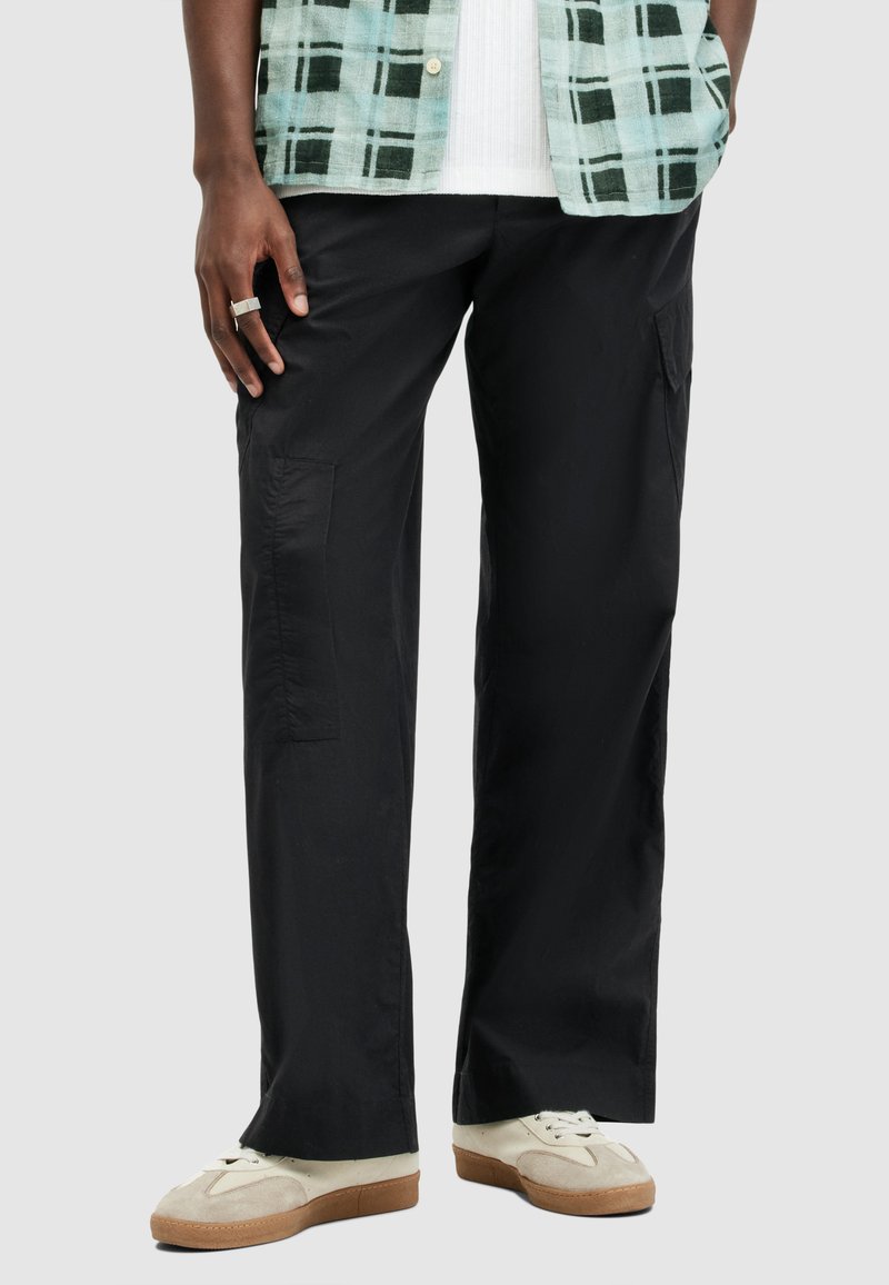 Pantalons cargo noirs avec une coupe ample, dotés de poches latérales et d'une texture lisse. Associés à des baskets claires et une chemise à carreaux.