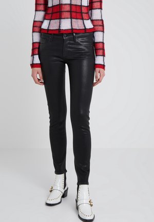 Osoba nosząca błyszczące czarne obcisłe spodnie, czerwono-białą koszulę w kratę z długim rękawem oraz białe botki na kostkę ze złotymi ćwiekami i klamrami.