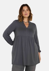 Graue Langarm-Tunika mit V-Ausschnitt und gerafftem Bund. Hergestellt aus weichem Stoff, mit dezenten NähteDetails und einer fließenden Silhouette.