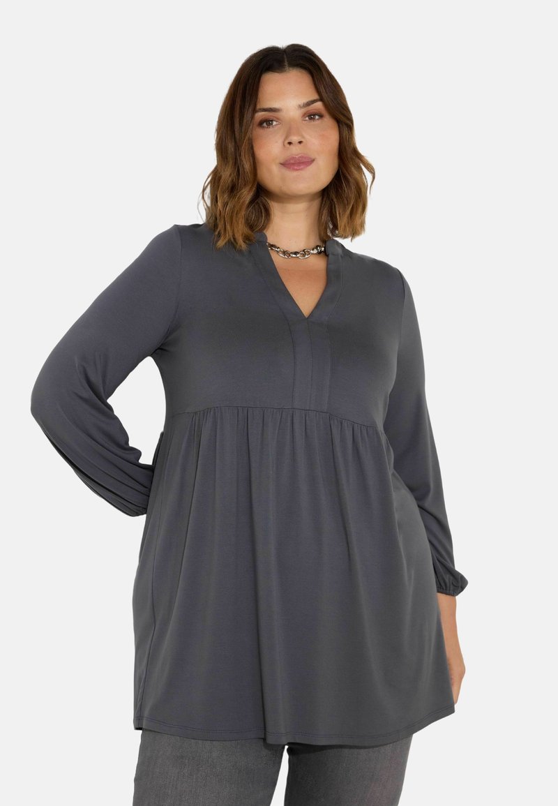 Graue Langarm-Tunika mit V-Ausschnitt und gerafftem Bund. Hergestellt aus weichem Stoff, mit dezenten NähteDetails und einer fließenden Silhouette.