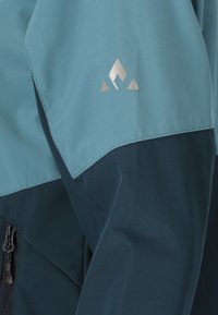 Waterproof jacket featuring a blue and dark navy color scheme, smooth texture, minimalistic design, and a silver logo on the shoulder.