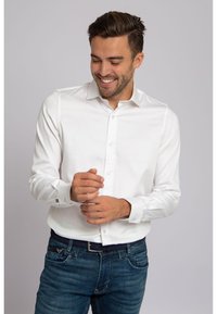 Wit overhemd met lange mouwen, een spreidkraag, knoopsluiting aan de voorkant en manchetten met één knoop, gecombineerd met een blauwe spijkerbroek en een donkere riem.