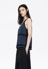 Top in tessuto navy con dettagli in pizzo nero lungo i lati e sull'orlo inferiore. Presenta uno scollo a U e una vestibilità comoda. Abbinate a pantaloni neri.