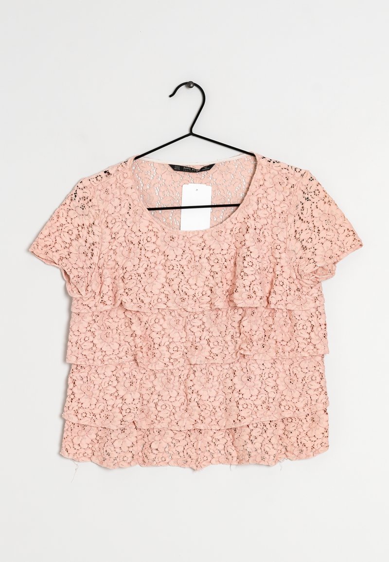 Roze kanttop met een ronde halslijn en korte mouwen, met drie lagen kant in verschillende bloemenpatronen. Hangt aan een zwarte haak.