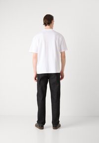 Hvit kortermet polo med mørkegrå rette bukser, kjennetegnet av et minimalistisk design uten synlige mønstre eller dekorasjoner.