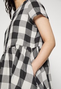 Robe à carreaux noir et blanc en tissu léger, avec des manches courtes, une jupe texturée à volants et des poches latérales.