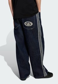 Temno modre ohlapne kavbojke iz jeansa s tremi sivimi črtami ob straneh in vezenim logotipom na zadnjem žepu.