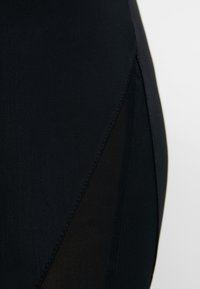 Crne kupaće gaće s elegantnim dizajnom, sa prozirnom mrežastom panelom sa strane i glatkim teksturiranim materijalom.