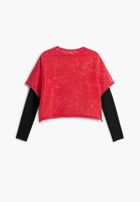 Punane lühendatud t-särk kulunud tekstuuriga, lühikeste varrukatega, must pika varrukaga aluskiht ribilise mustriga.