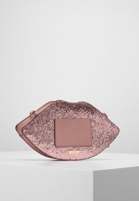 Käsilaukku muodoltaan huulille, vaaleanpunaisesta keinonahasta, jossa on kimaltava ruusukultainen pinta. Laukussa on neliöpaneeli ja kultainen logoelementti.