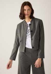 Grau gestreifter, kurzer Blazer mit rundem Ausschnitt, Ein-Knopf-Verschluss und zwei Fronttaschen, kombiniert mit einem weißen T-Shirt mit Grafik.