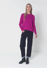 Magenta Langarmshirt mit lockerem Schnitt, kombiniert mit dunkelblauen umgeschlagenen Jeans und schwarzen Ankle Boots. Schlichtes Design, weiche Textur.