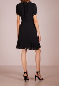 Černé šaty s krátkými nabíranými rukávy, vyšívanými detaily na rukávech a lemu, širokou sukní, vyrobené z lehkého materiálu. Nošeny s černými podpatky.