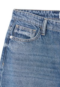 Jeans jeansowe w wyblakłym niebieskim odcieniu, z małą przednią kieszenią, mosiężnym guzikiem i kontrastującym żółtym wykończeniem na szwach.