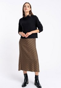 Czarny sweter dzianinowy z kominem, zestawiony z brązową spódnicą midi w czarny abstrakcyjny wzór. Całość dopełniają czarne botki za kostkę.