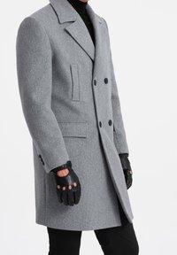 Šedý vlněný kabát s dvouřadými knoflíky, klopovým límcem s výstřihem, dvěma bočními kapsami a texturovanou tkaninou. Nositelným černým rukavicím bez prstů.