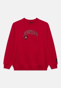 Κόκκινο φούτερ με στρογγυλή λαιμόκοψη και μακριά μανίκια, με την επιγραφή «JORDAN» και λογότυπο μπάσκετ στο στήθος, καθώς και μια μικρή μαύρη ετικέτα λογότυπου στο μανίκι.