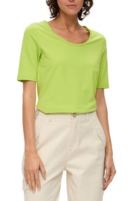 Felle limoengroene T-shirt met korte mouwen en een brede ronde hals, gecombineerd met lichtbeige broek met zijzakken.