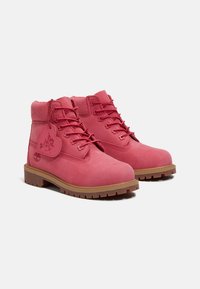 Stivali alla caviglia in pelle rosa con punta rotonda, cuciture in rilievo, sei paia di occhielli e suola in gomma; presentano un'etichetta a forma di cuore e un logo.