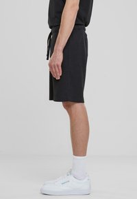 Shorts en coton noir avec une coupe décontractée, taille à cordon, et une longueur jusqu'aux genoux, associés à des baskets blanches et des chaussettes mi-mollet.