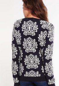 Granatowy sweter z dzianiny z białymi wzorami kwiatowymi, z długimi rękawami i prążkowanym dołem z misternymi detalami.