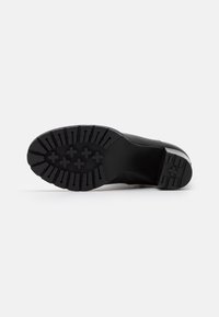 Suela de zapato negra con una superficie de goma texturizada que presenta surcos multidireccionales y elementos elevados para tracción y agarre.
