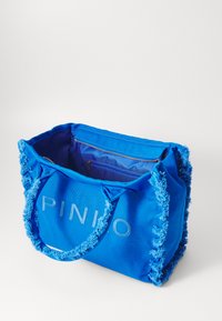 Sininen kangaskassi, jossa on teksturoitu pehmeä yksityiskohta reunoilla ja vetoketjullinen sisätasku. Painettuna "PINIO" vaaleansinisellä.
