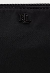 Juodas nailono maišelis su tekstūruota paviršiumi, užtrauktuko uždarymu ir iškaltu "RL" logotipu kampe, skirto prekės ženklui.