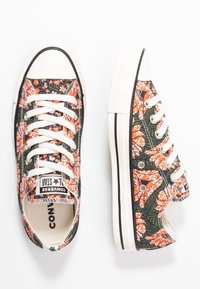 Baskets en toile avec un motif floral orange et blanc sur fond vert foncé. Lacets blancs et capuchon en caoutchouc. Accents de semelle noire.