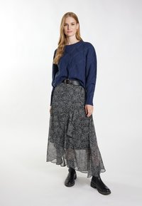 Marineblauwe gebreide trui met diamantpatroon, gecombineerd met een vloeiende zwarte rok met een cirkelvormig paisley ontwerp. Zwarte enkellaarsjes.