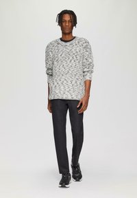 Grau-weißer, strukturierten Strickpullover mit langen Ärmeln, kombiniert mit dunkelblauen Slim-Fit-Hosen und schwarzen Sneakers. Schlichtes, modernes Design.