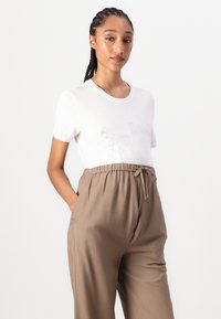 T-shirt blanc à col rond avec un motif en strass, associé à un pantalon beige ample avec une taille élastique.