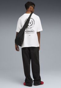 Biała, oversize'owa koszulka bawełniana z czarnym nadrukiem na plecach, połączona z czarnymi szerokimi spodniami i czerwonymi sneakersami oraz czarną torbą na ramię.