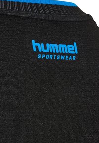 Gros plan sur un tissu noir avec le logo bleu « hummel SPORTSWEAR » près d'un col côtelé aux rayures bleues et noires.