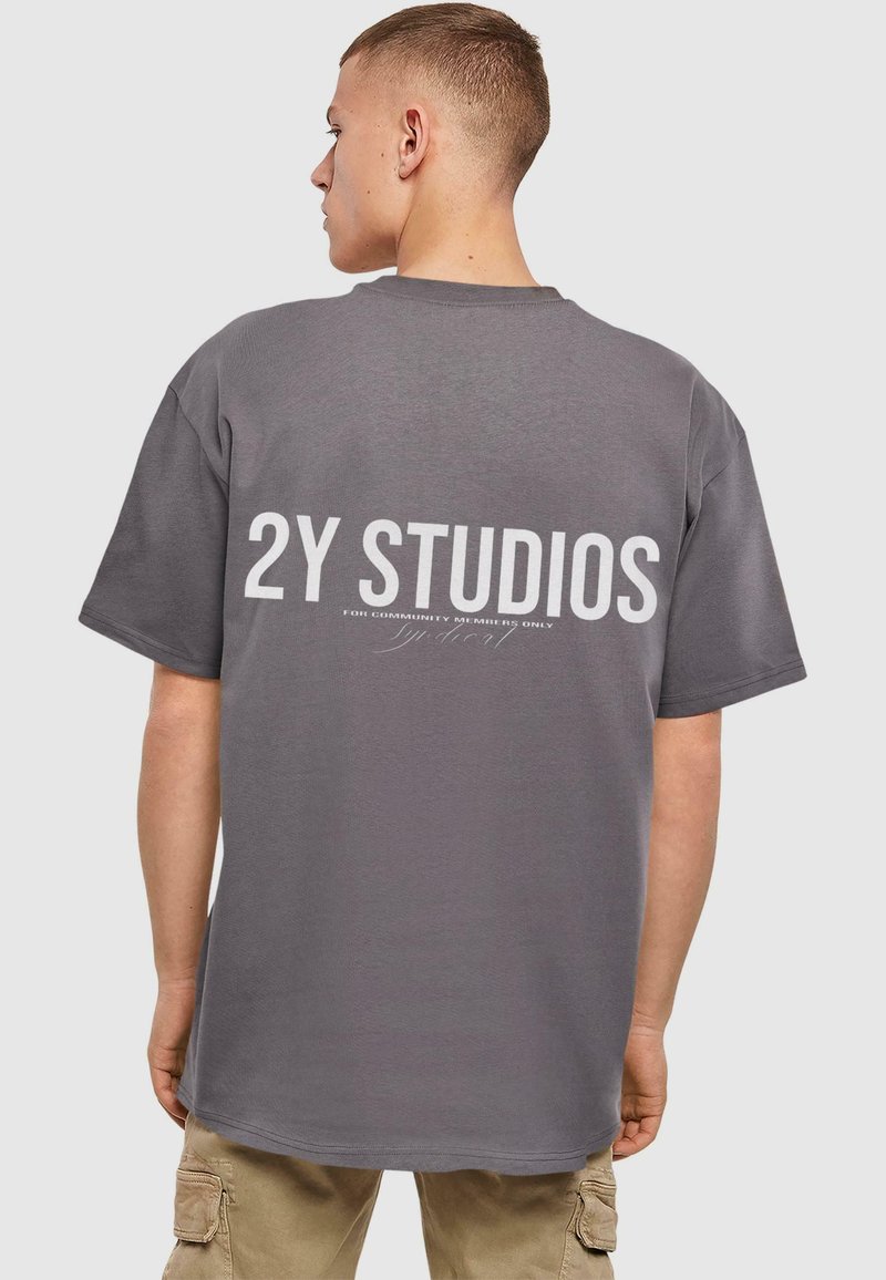 Pelēks īsā piedurkne T-krekls ar uzrakstu "2Y STUDIOS" lielos baltos burtiem aizmugurē, izgatavots no mīksta kokvilnas auduma.
