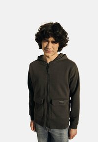 Sweatshirt zippé gris foncé avec une fermeture éclair à l'avant et deux poches avant. Tissu doux et poignets côtelés, avec un petit patch de la marque sur la poche.