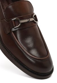 Leather loafers in dark brown featuring a smooth finish, silver hardware accent, and a raised seam along the sole for detail.