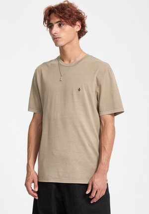 Beige Baumwoll-T-Shirt mit Rundhalsausschnitt und kurzen Ärmeln, mit einem kleinen schwarzen Logo auf der linken Brust. Glatte Textur, lässige Passform.