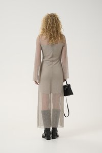 Sheer long dress in light gray with floral pattern, long sleeves, fitted bodice, and flowing skirt. Worn with black ankle boots and handbag.