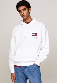 Felpa bianca con cappuccio, dotata di tasca frontale e cordoncino, con un logo decorativo con dettagli in blu navy e rosso. Abbinale a jeans in denim blu.