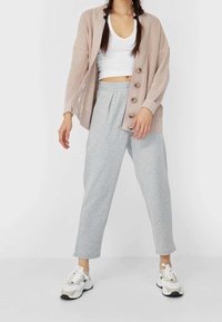 Ljust rosa stickad cardigan med stora knappar, matchad med grå tapered sweatpants och chunky vita sneakers med neutrala accentfärger.