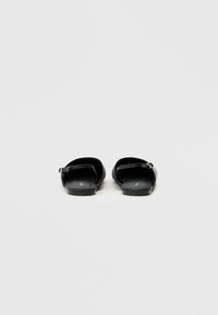 Czarne płaskie sandały z gładkiej skóry, z otwartym tyłem oraz cienkim paskiem przy kostce z metalową klamrą. Minimalistyczny design, bez wzorów.