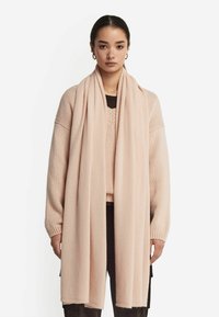 Lyserød tørklæde lavet af blødt stof, med en lang, rektangulær form og en glat tekstur samt rene kanter. Båret draperet over en sweater.