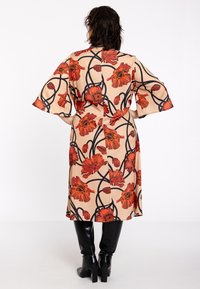 Beige kimono-stijl jurk met een bloemmotief in rood en zwarte omlijning. Heeft klokkende mouwen en een semi-aansluitende vorm.