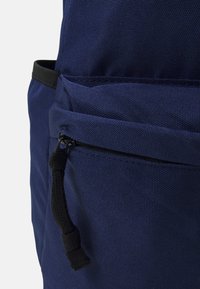 Zaino blu navy realizzato in tessuto textured, con una tasca frontale con zip e un'accente di cordino nero.