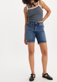 Džínové šortky v tmavě modré barvě s vysokým pasem a ohrnutými lemy, v kombinaci se pruhovaným tílkem a černými sandály na pásky.